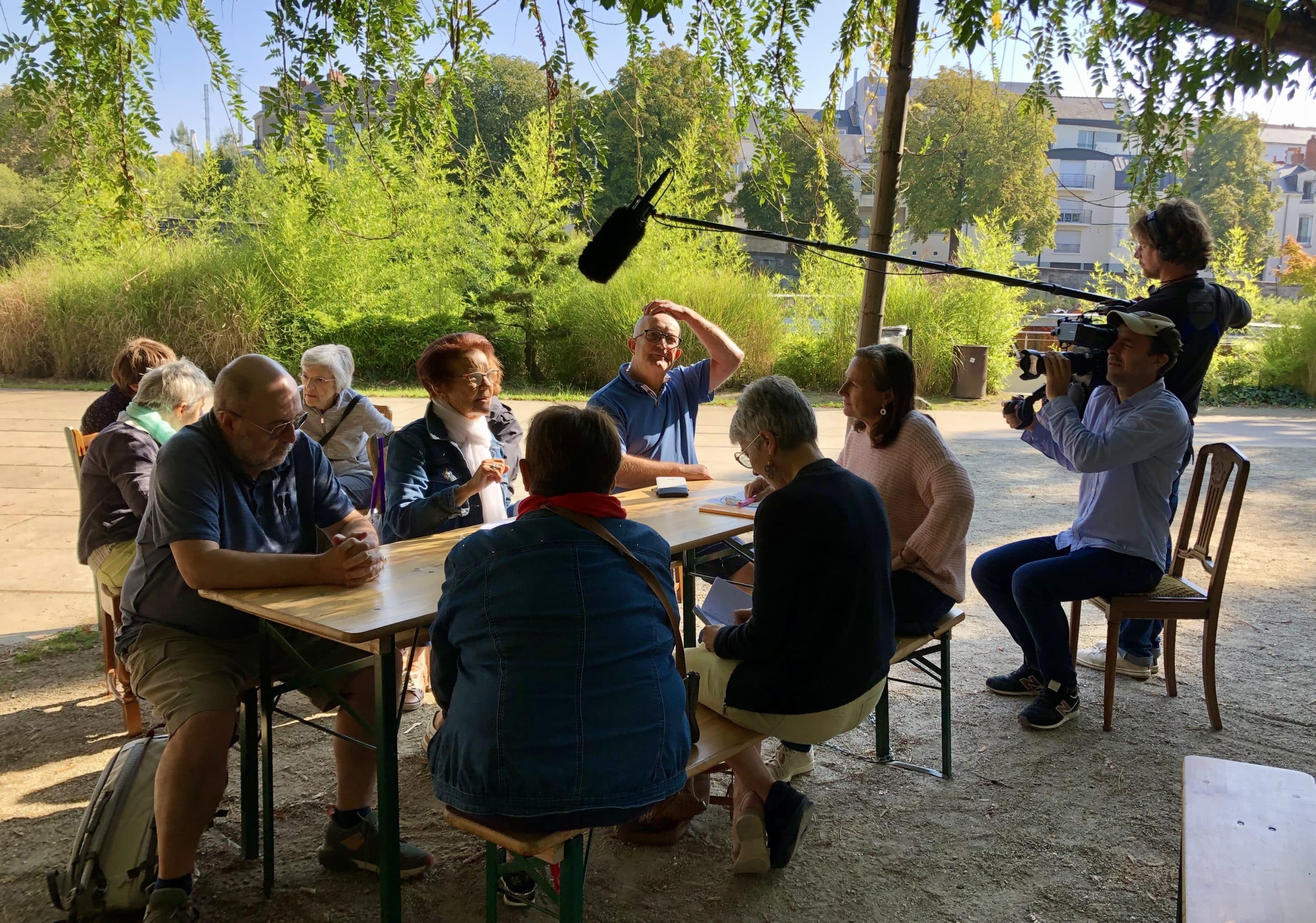 groupe de personnes à une table dehors avec une équipe de tournage